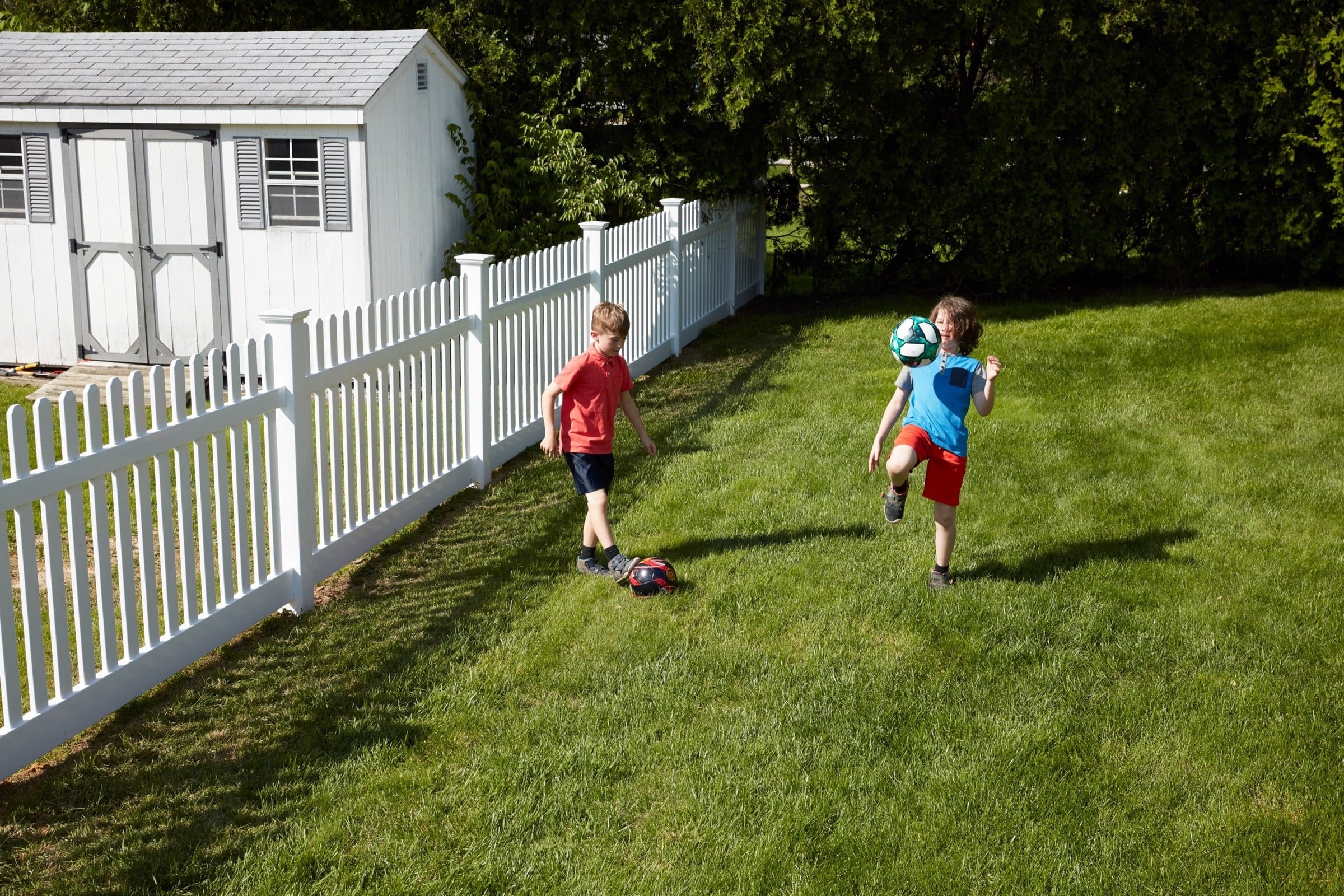 Two kids kicking a soccer ball in front of an activeyards fence